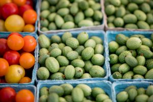 Pints of green cucamelons next to red and yellow cherry tomatoes