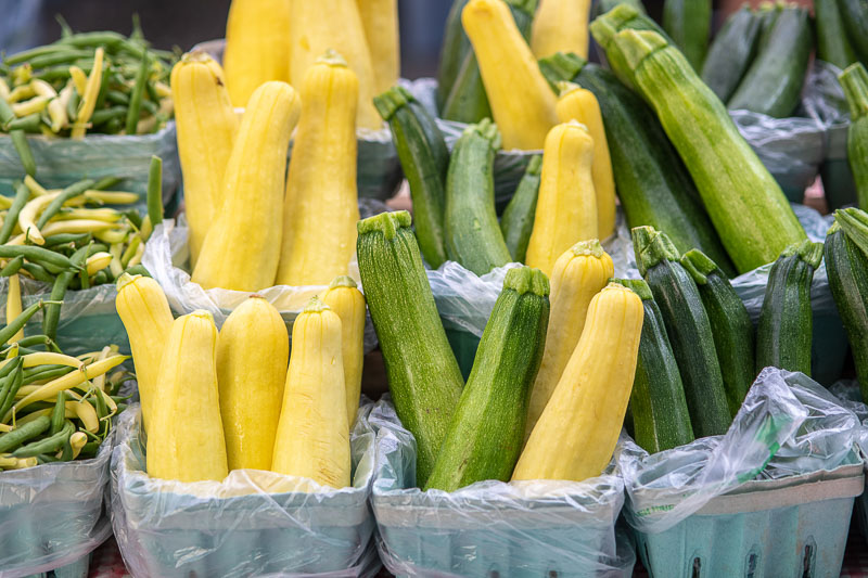 yellow squash and green zucchini standing up in quart size containers at a farmers' market